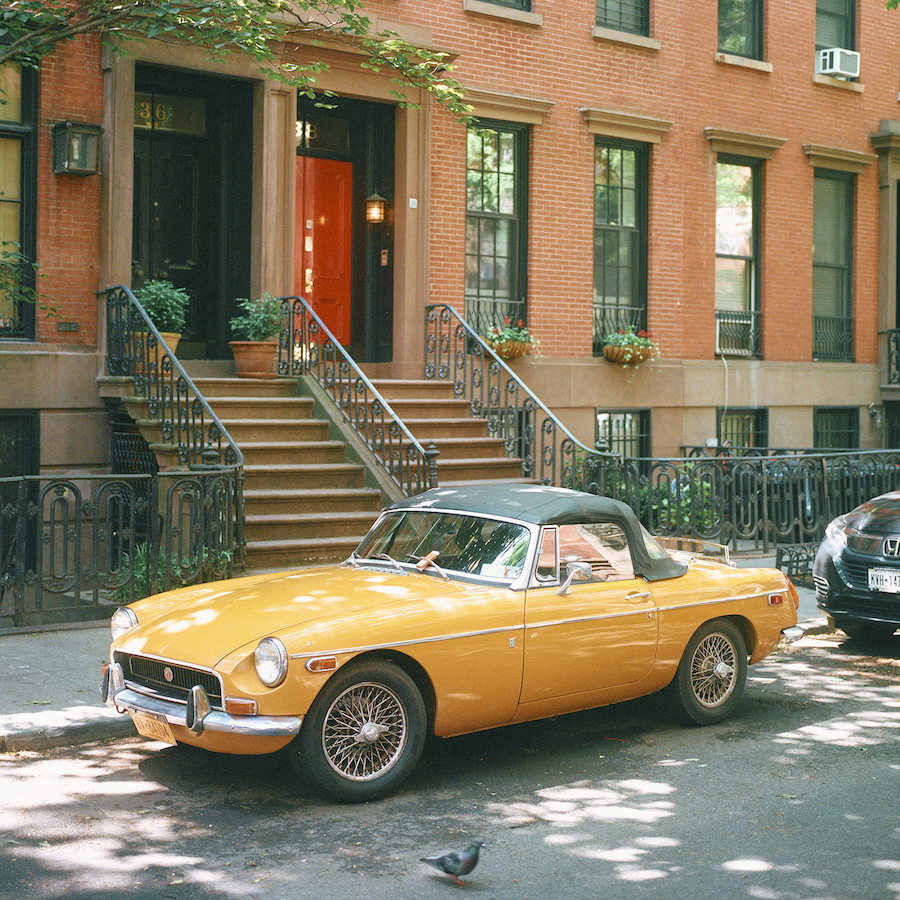 A Yellow Convertible Sports Car Is Parked In Front Of An Apartment Building Near A Bird In The Street